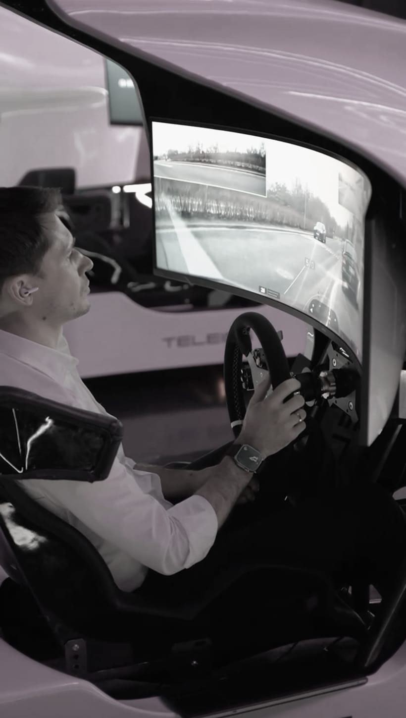A remote driver at the wheel of a Qibus driving station, a live road view on the curved screen